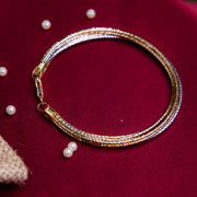 A tricolor 7-layered bracelet made of sterling silver in rose gold, silver and gold color, displayed on a red background with some pearls scattered around.